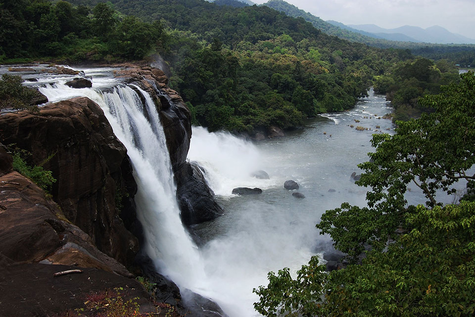 water gushes down the athirappilly falls into the forest as viewed from the top of the waterfall