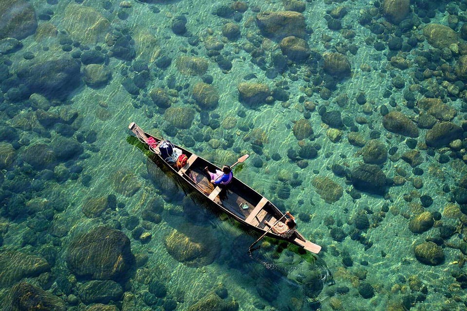 a top down view of tourists being rowed in a boat in crystal clear dawki river