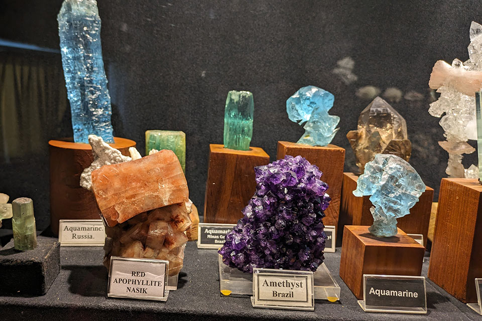 a close up view of some rare minerals such as amethyst from brazil, aquamarine from russia, and red apophyllite from nasik kept at gargoti museum