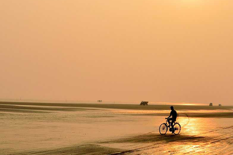 a person cycling on madarmani beach while sun sets in the background